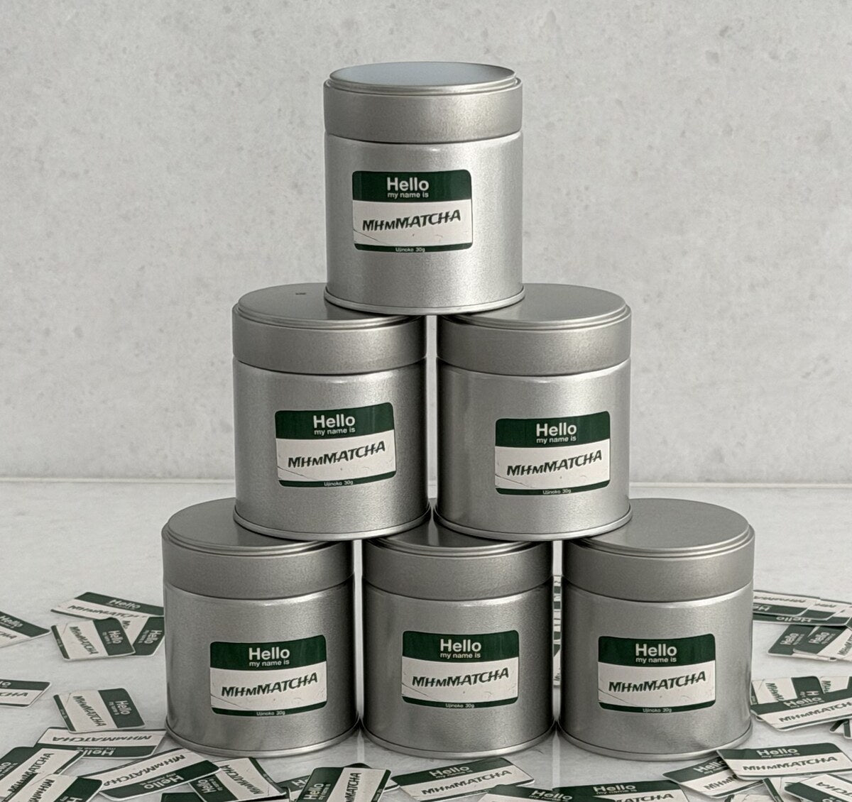 Six MhmMATCHA ceremonial matcha tins stacked in a pyramid with name-tag stickers